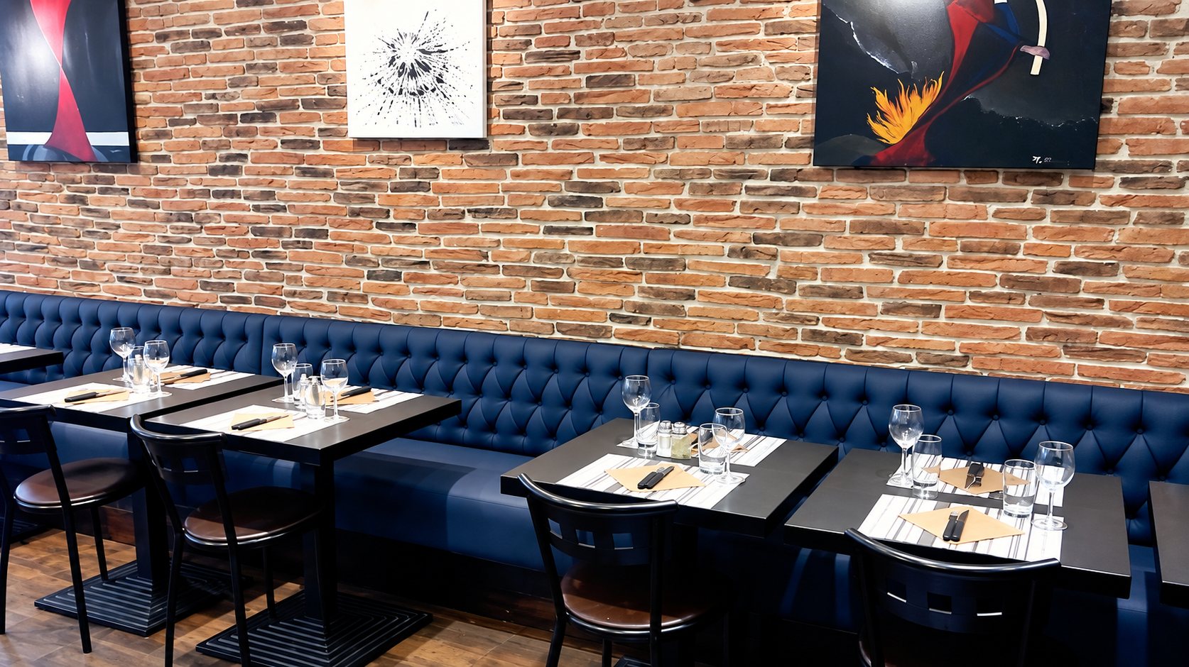 Salle du restaurant avec banquette bleue capitonnée et mur de briques